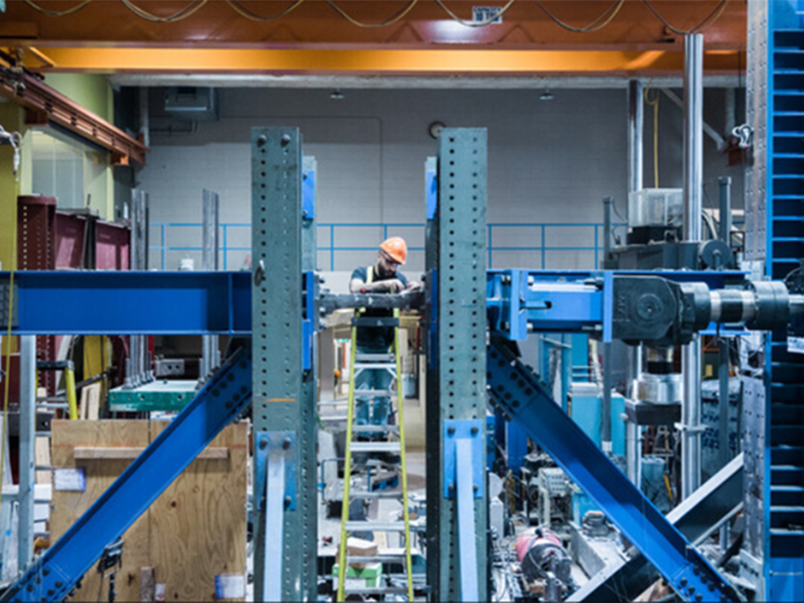 Man in hardhat placing a specimen in a large destructive testing machine.